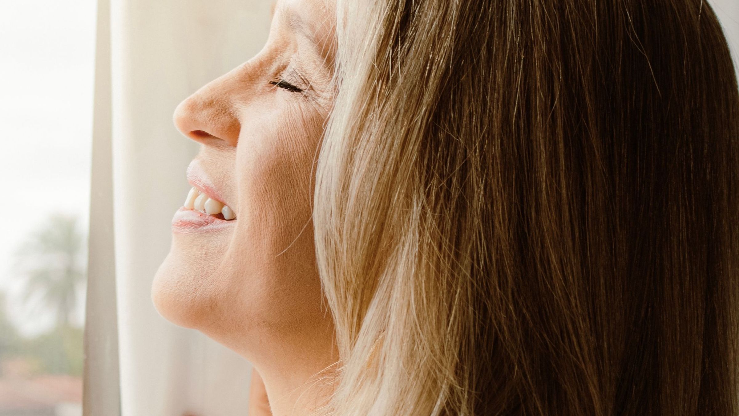 Une femme de profil, le visage tourné vers la lumière, sourire apaisé