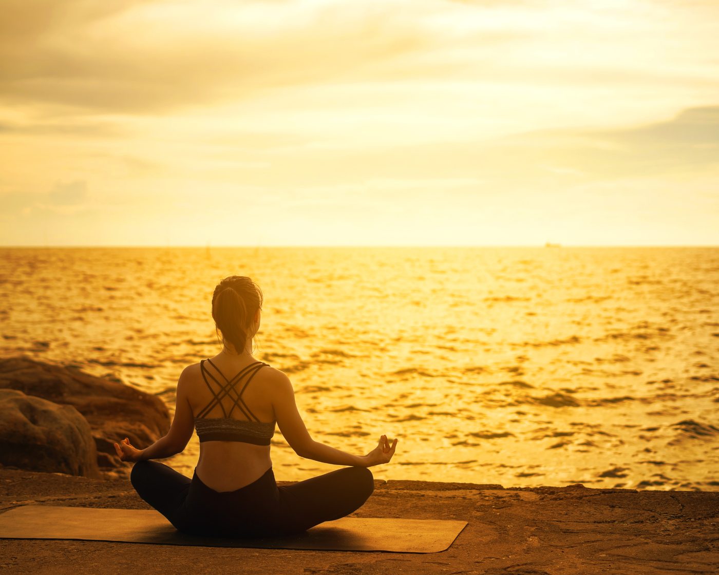 Une femme en méditation au bord de la mer, au soleil couchant